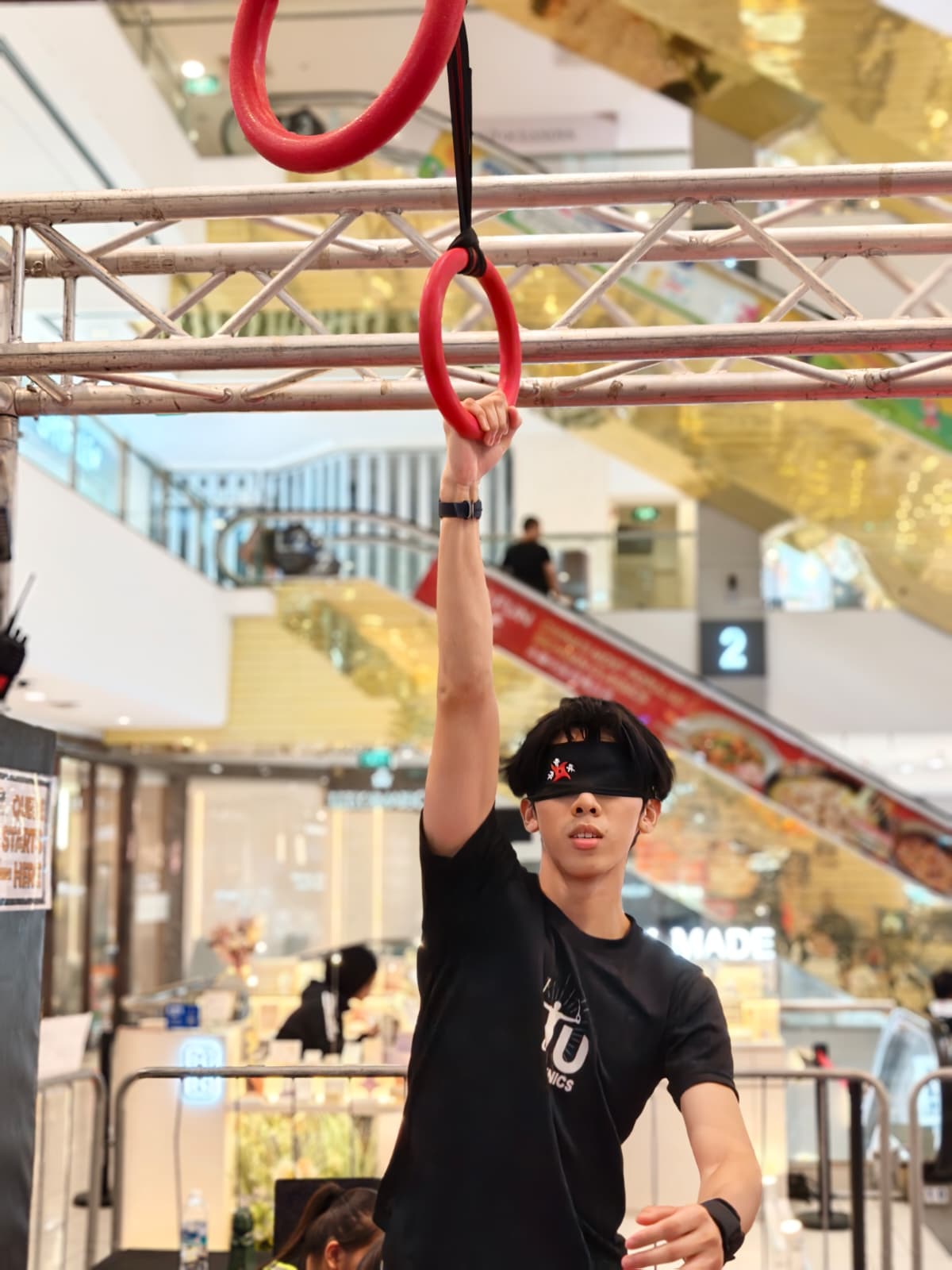 A blindfolded participant hanging from a ring in a mall atrium.