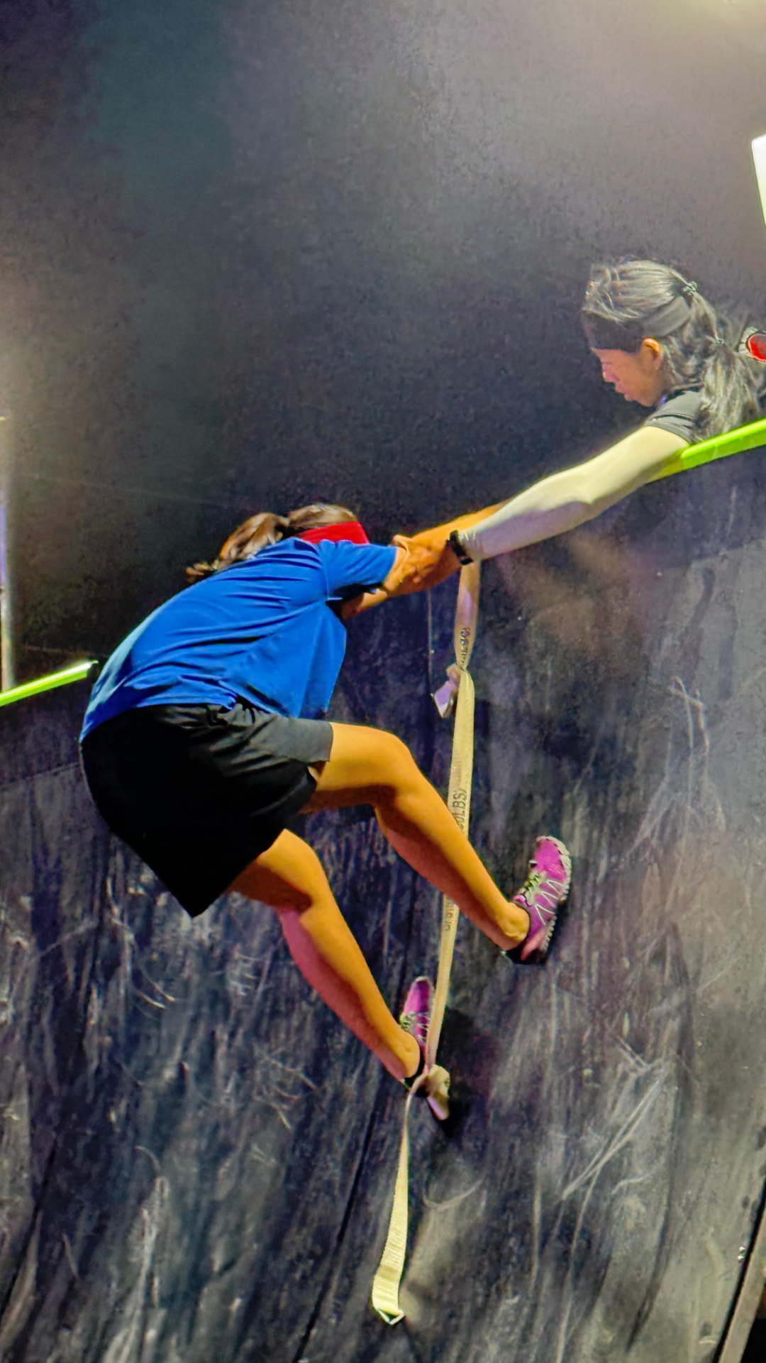 Two participants helping each other over a wall.