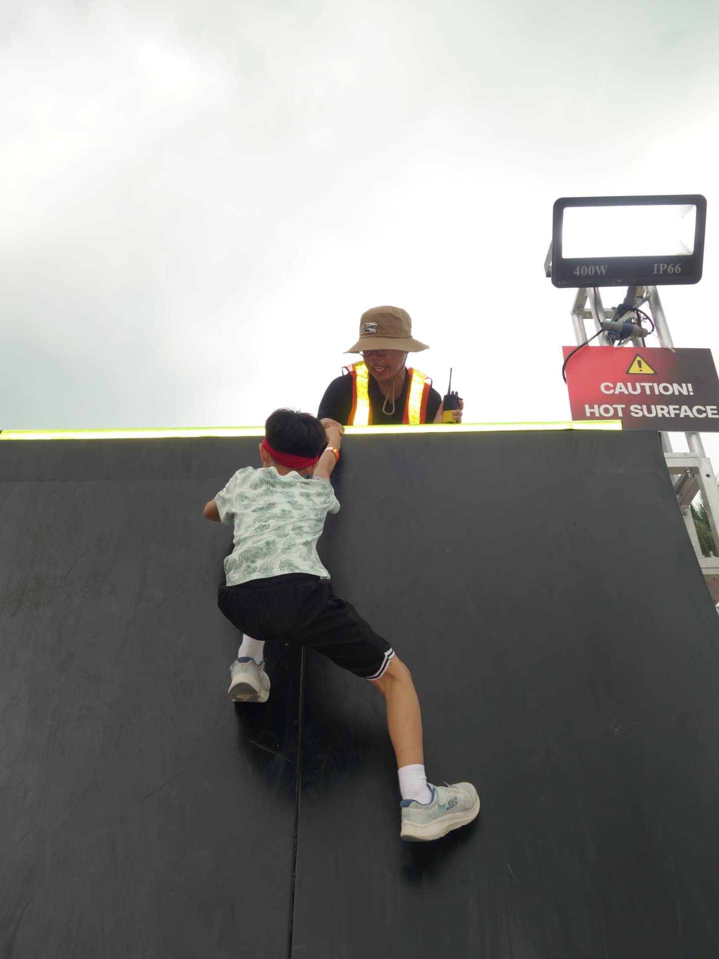 A boy reaching the top of a warped wall with a marshal pulling him over