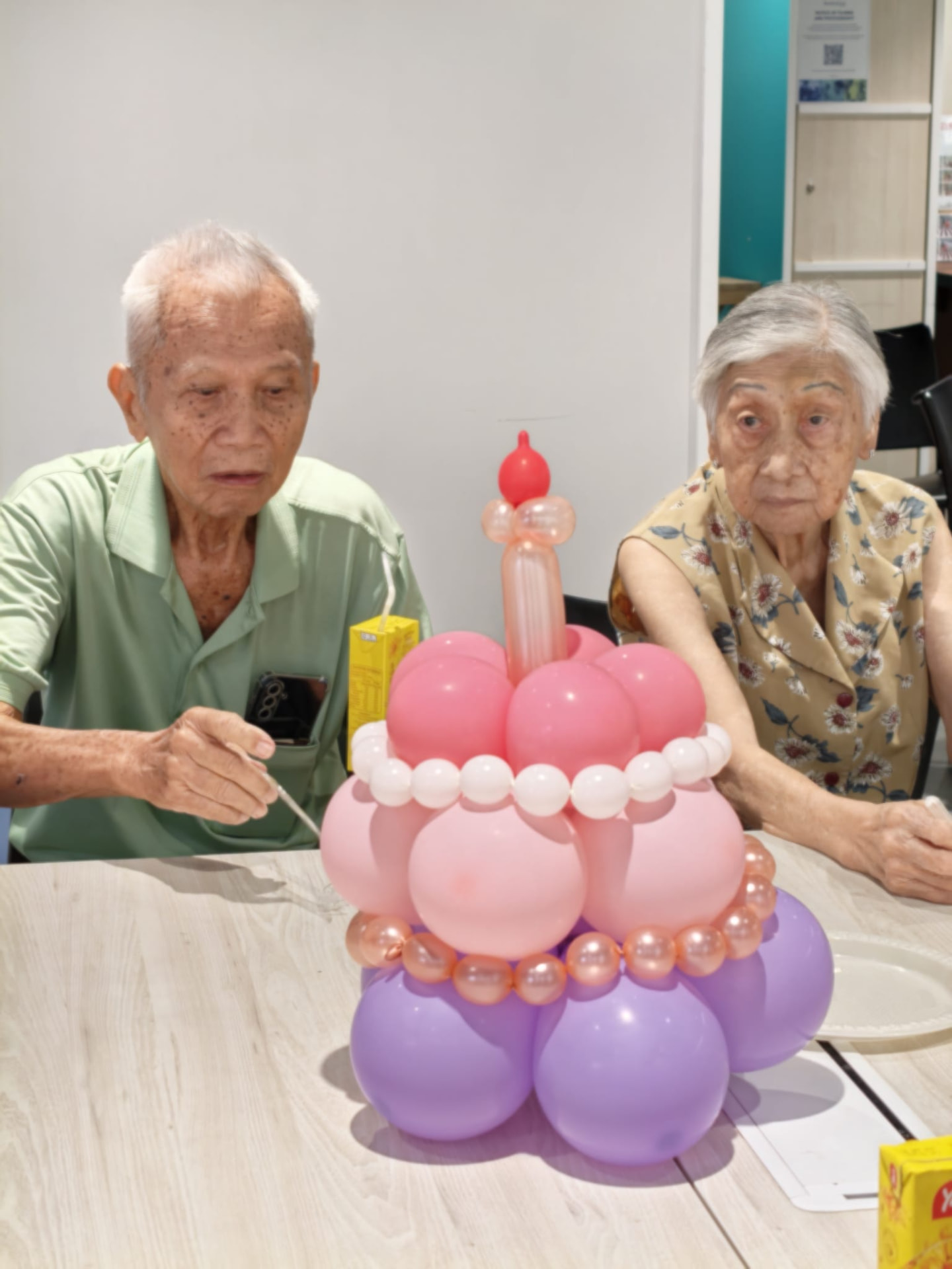 An older man and woman beside a colourful balloon birthday cake