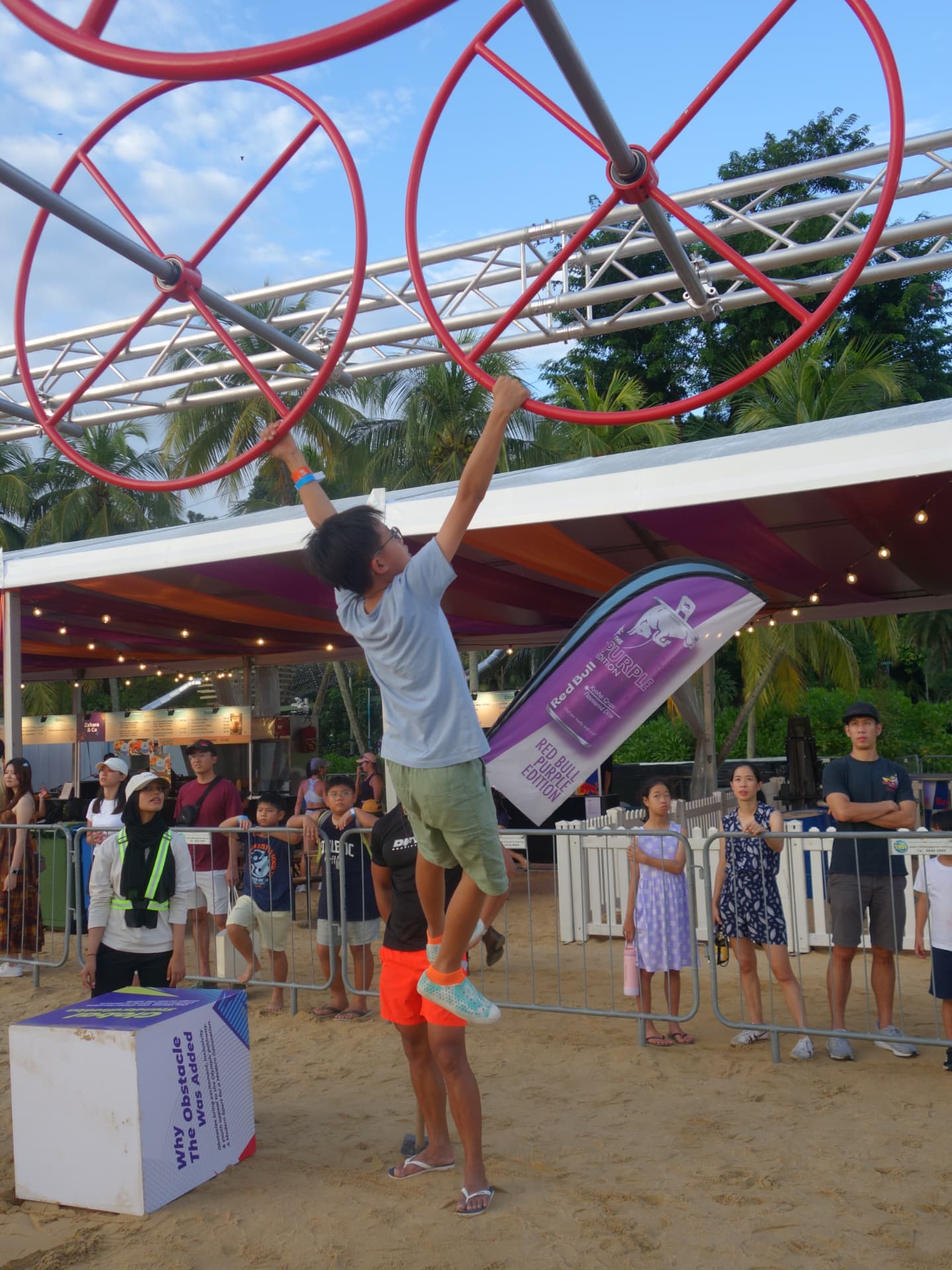A boy swinging between rings on an obstacle course while a crowd watches